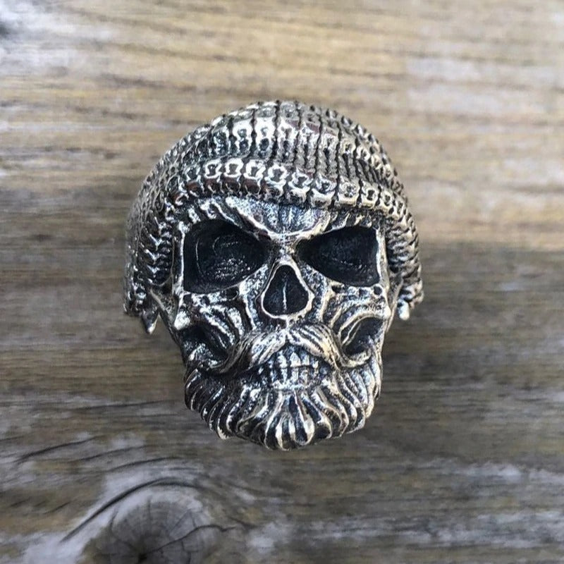 Bearded skull sterling silver ring front view on wooden surface, antiqued silver with retro gothic details and textured knit beanie design