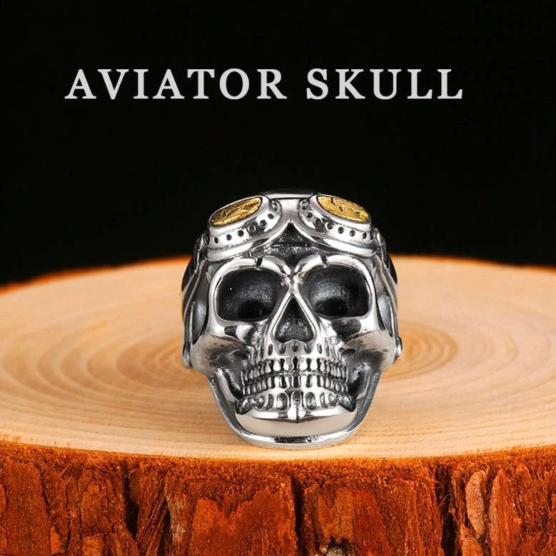 Aviator skull ring front display on wooden base showing intricate carved skull with pilot goggles and gold-toned lens accents
