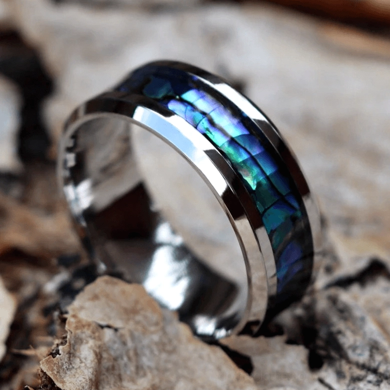 Unisex gothic abalone ring high angle side view on wooden bark surface showing silver trim and iridescent shell
