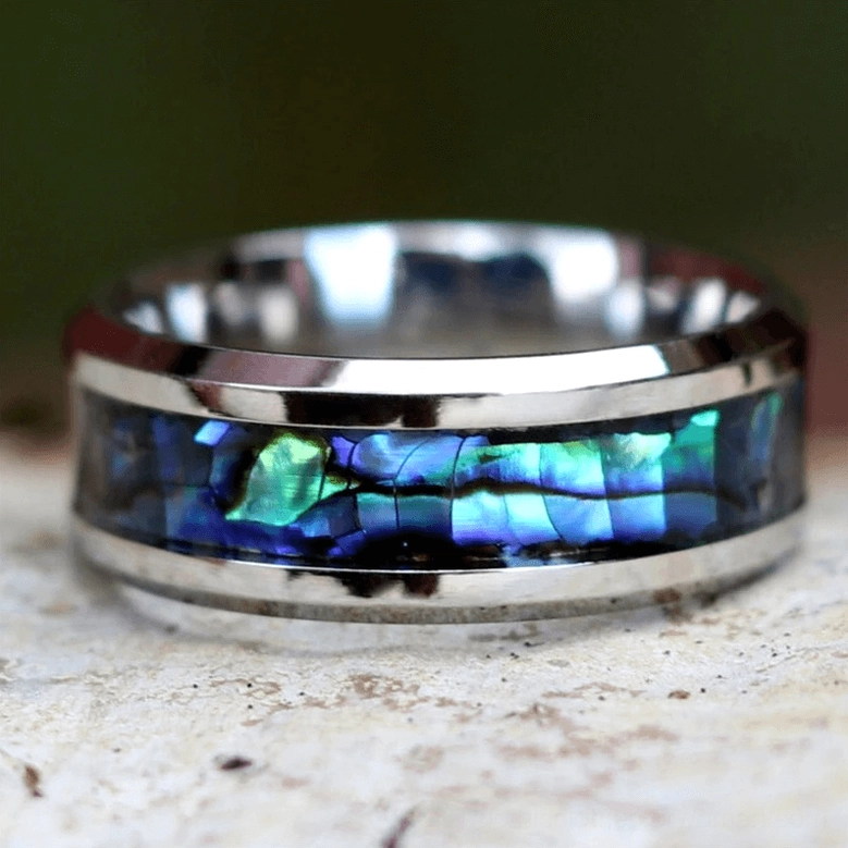 Iridescent abalone inlay ring flat lay view showing vivid blue-green shell pattern and polished stainless steel band
