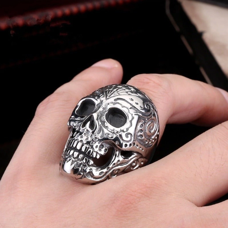 Engraved sugar skull ring worn on adult male hand front view against dark wooden background, showcasing gothic design and ring proportions