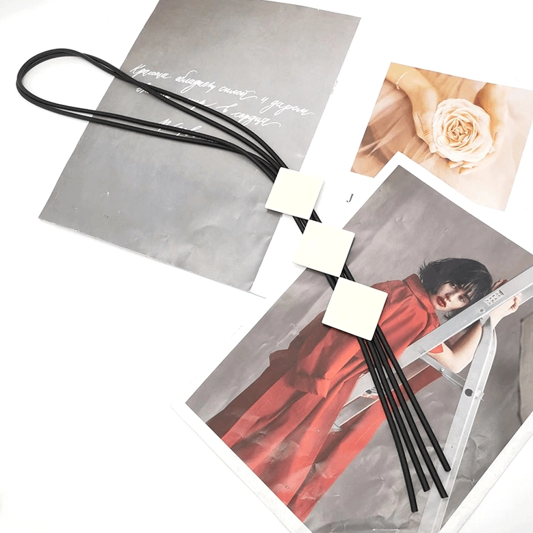 Minimalist long pendant necklace flat lay on vintage fashion prints background, three square wooden pendants with black tassel cord detail