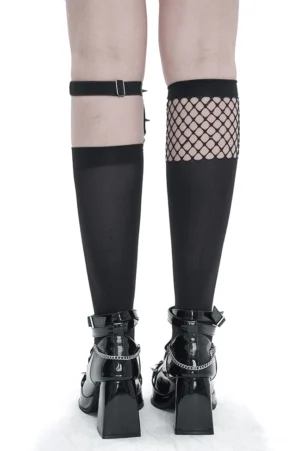 Mannequin legs displaying asymmetrical gothic knee-high socks with fishnet splice and metal heart buckle garter alongside platform boots