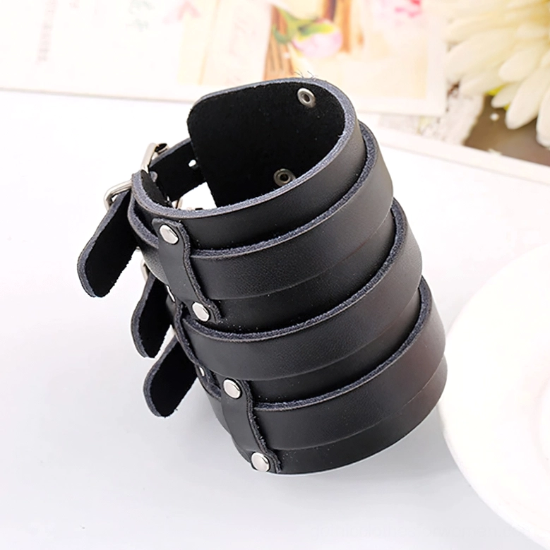 Top-left oblique view of black genuine leather cuff bracelet with adjustable buckles and silver rivets on decorative tabletop