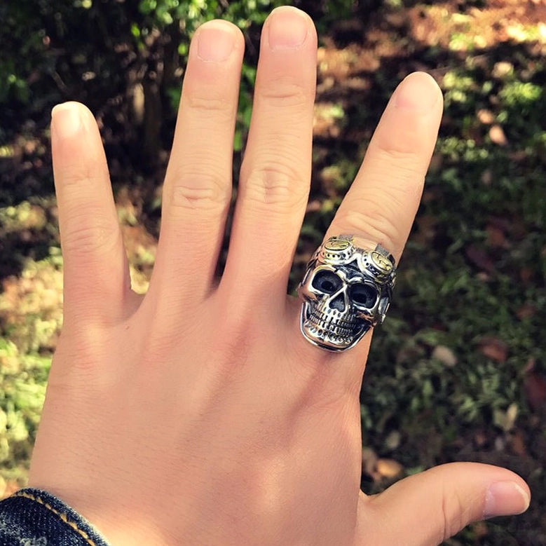 Male hand wearing aviator skull biker ring in outdoor woodland setting showing on-finger side view and gothic aesthetic