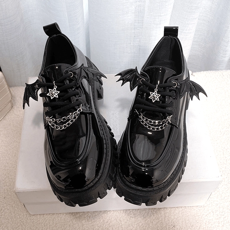 Overhead flat lay of black platform loafers with pentagram charm and bat wing metal trim, top-down front view showing lace-up closure