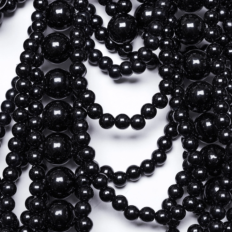 Macro detail of glossy black pearl strands and metal chain clasp showing craftsmanship and material quality
