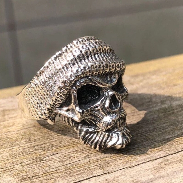 Gothic skull ring three-quarter side view on wooden table, showing detailed beard carving and knitted beanie texture on 925 sterling silver