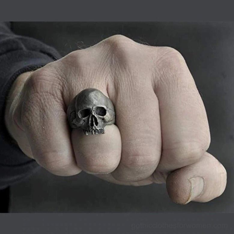 Biker skull ring on male middle finger, front view with grey studio background