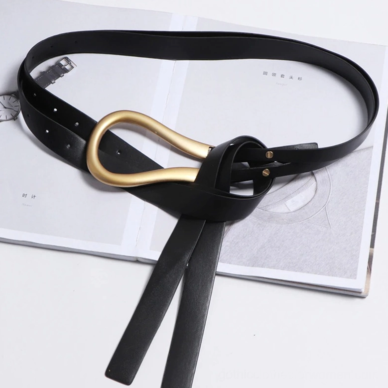 Coiled black PU leather belt overhead flat lay showing full length, gold buckle and adjustment holes, professional product presentation on magazine