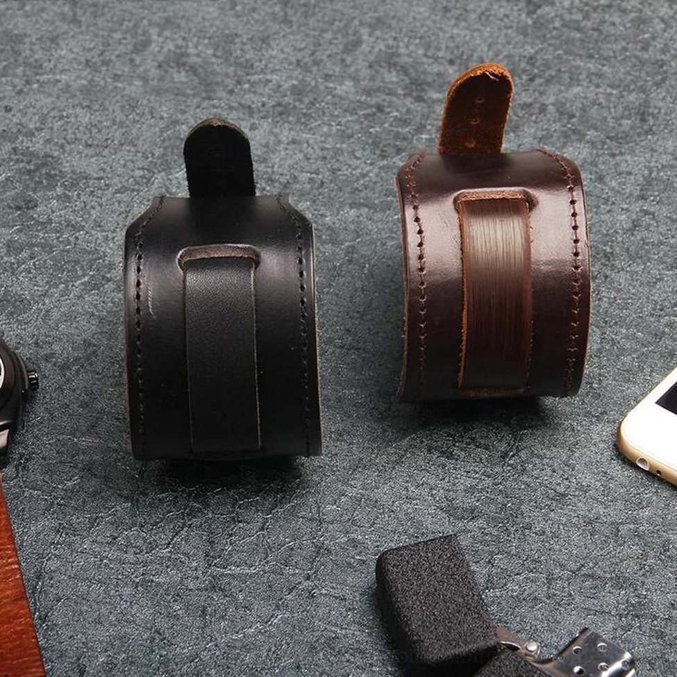 Overhead flat lay of black and brown wide leather gothic bracelets with smartphone and lighter on dark textured surface, showing both color options
