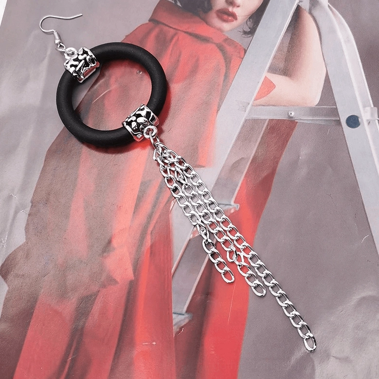 Black rubber drop earring with long double silver chain tassel on female model, flat lay with red clothing background, alternative jewelry