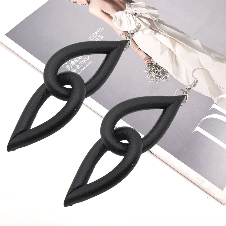 Black handmade rubber earrings worn on partial female model figure against magazine background, showing lightweight interlocking teardrop links in styling context