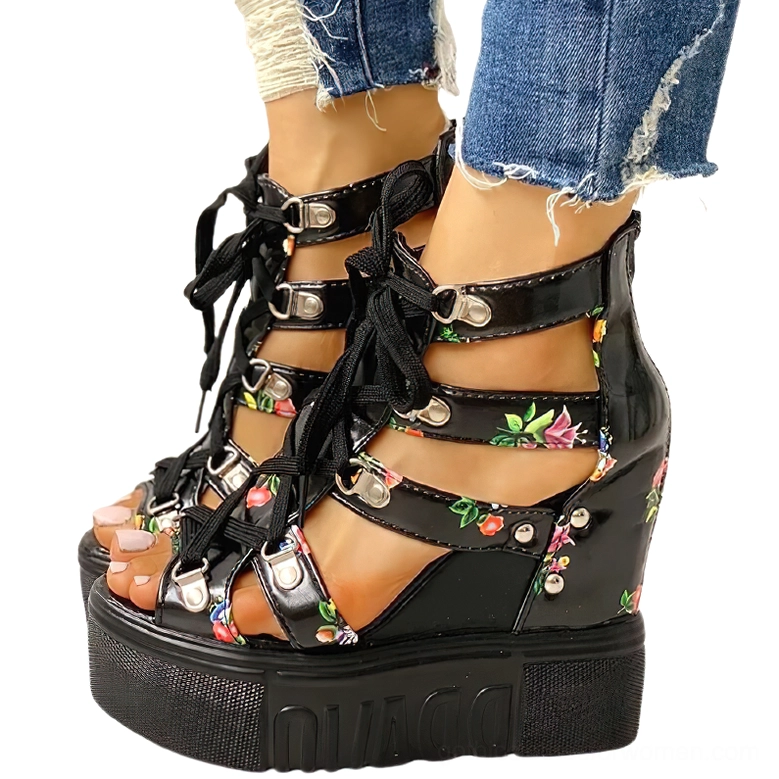 Black floral platform wedge gladiator sandals with lace-up front and buckle ankle straps, shown on model wearing ripped denim jeans