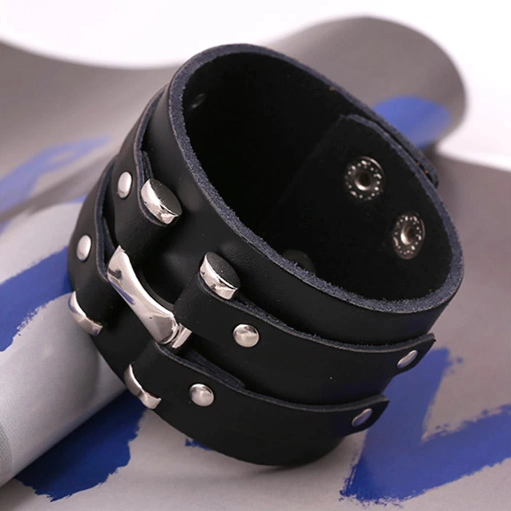 Black leather wrist cuff bracelet low-angle display, featuring silver metal hardware details and snap button fasteners on dark background