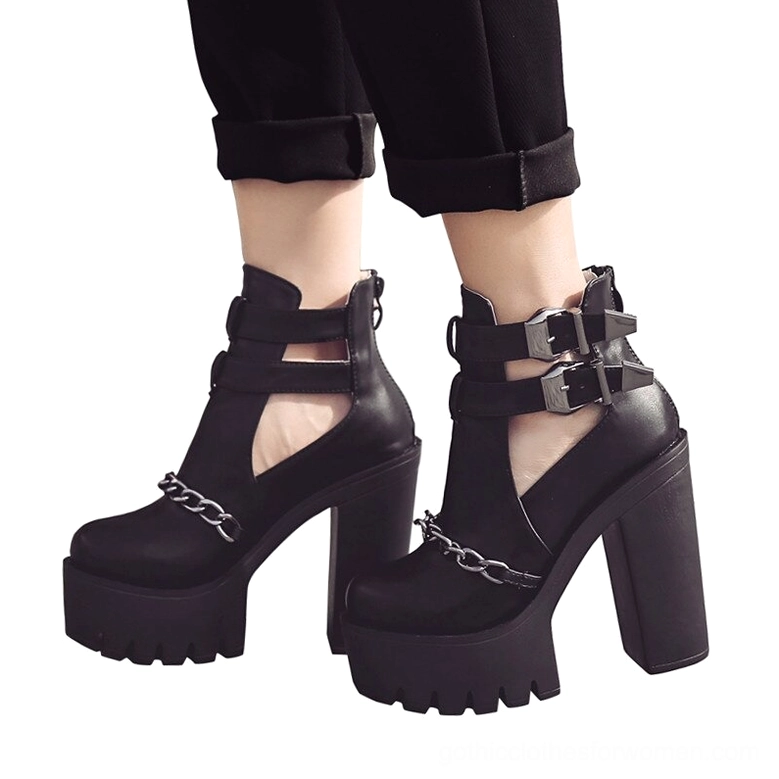 Pair of black gothic platform boots on model's feet front three-quarter view with cutout ankle and metal chain decoration
