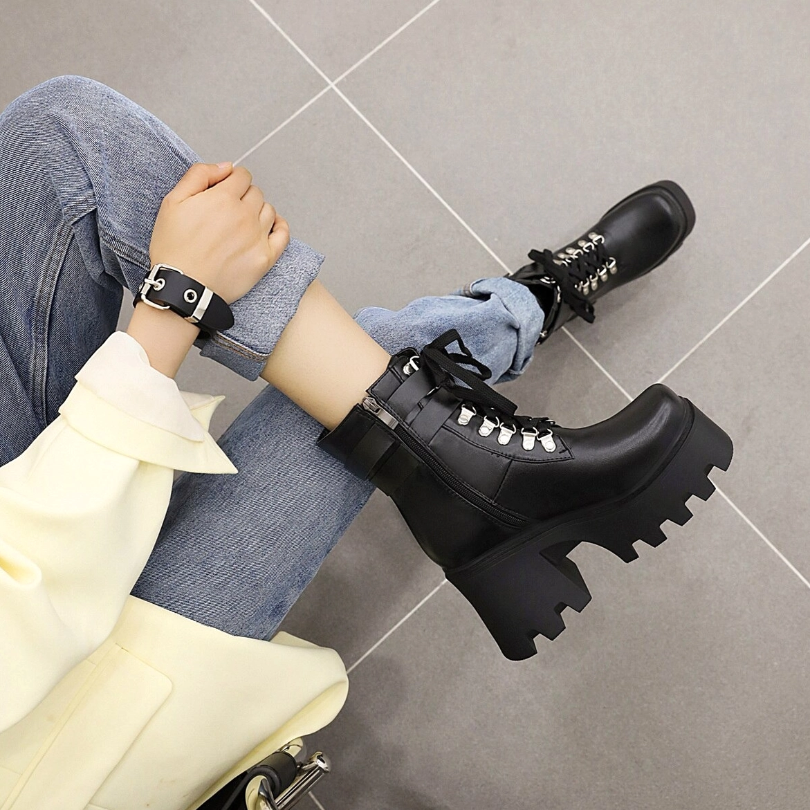 Black gothic platform combat boots styled with yellow coat, seated overhead view showing the decorative fretwork and buckle details