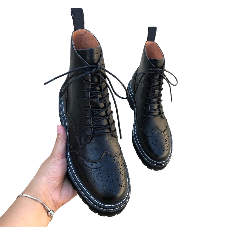 Pair of black leather gothic brogue boots worn in hand, showing lace-up fastening, brogue details, and chunky lug sole