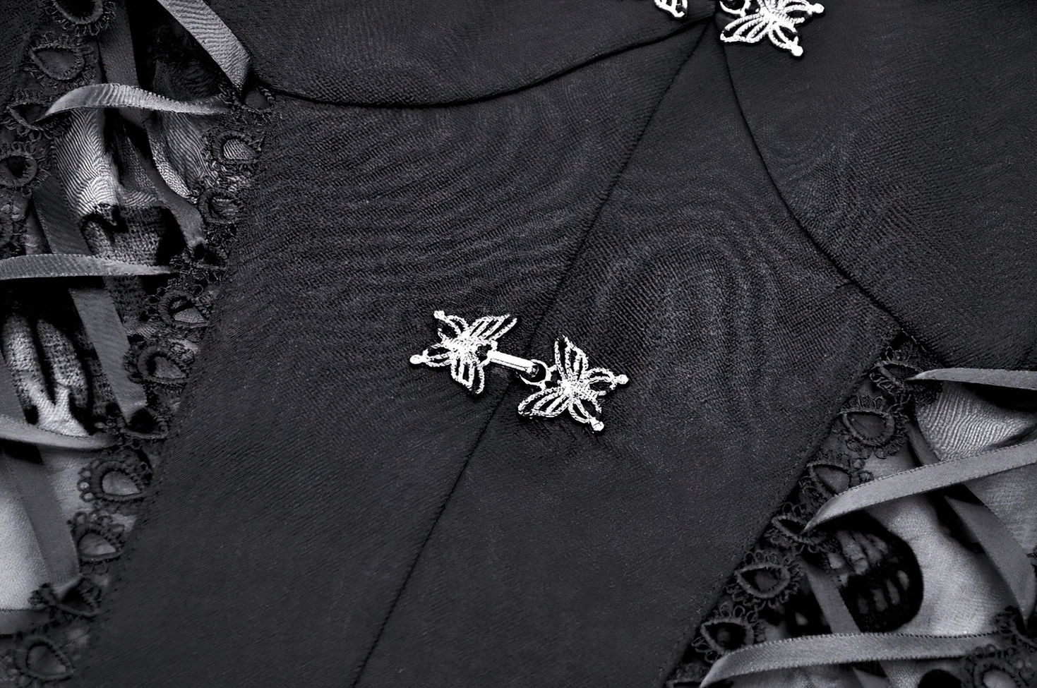 Macro close-up of metal butterfly-shaped buckles on black gothic dress with delicate lace trim