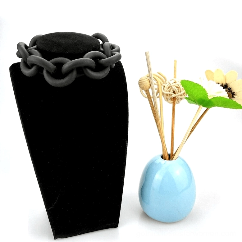 Black matte rubber chain bangle displayed on black velvet jewelry stand, front view showing architectural linked chain structure