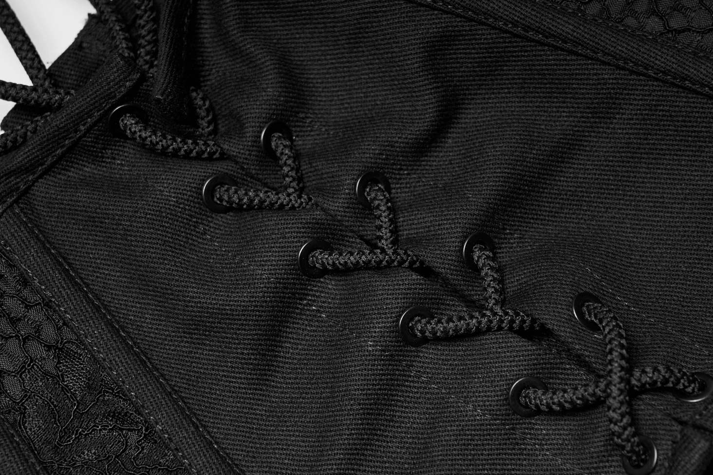 Close-up detail of black gothic corset lace-up closure showing black lace ties, fabric eyelets, and woven construction of back fastening system