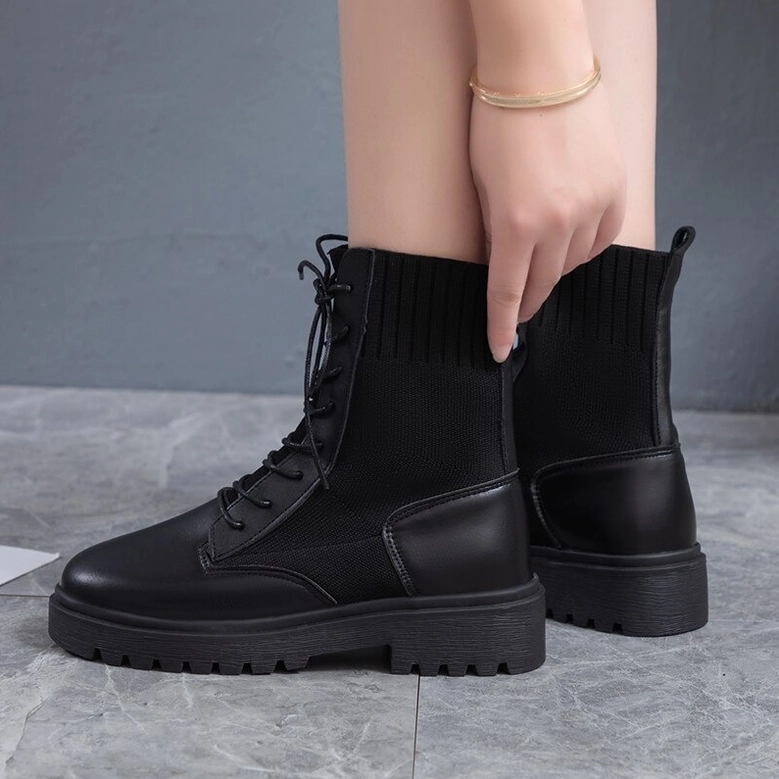 Woman wearing black platform gothic combat boots - lace-up ankle boots side view with gold jewelry on grey wall