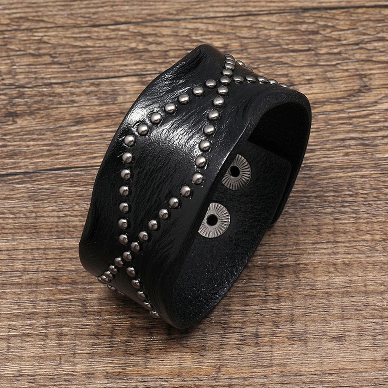 Black leather gothic cuff bracelet with geometric rivet studding, oblique angle showing width and hardware details on wooden surface