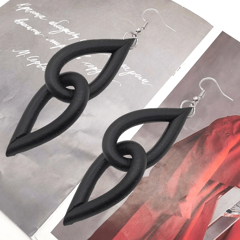 Pair of black interlocking link dangle earrings on magazine page background, displaying matte finish and architectural teardrop design