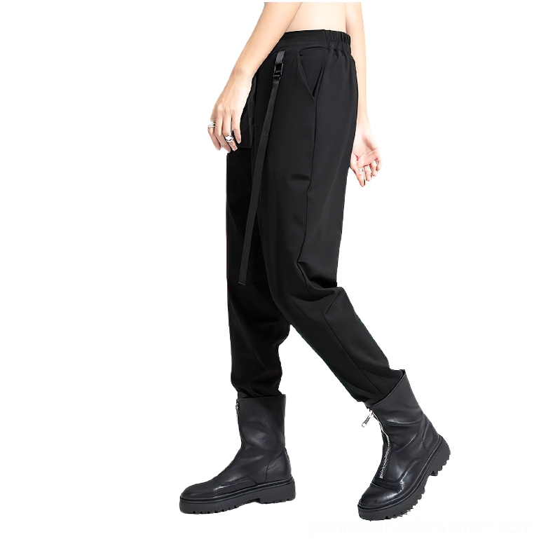 Side profile of black tapered harem trousers showing elastic waist, side ribbon, and ankle cuff hem on model wearing combat boots