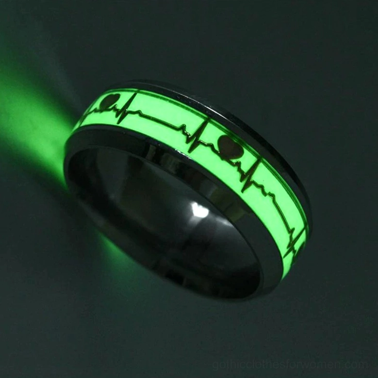 Single black metal luminous ECG heartbeat ring, close-up side view in darkness showing intense bright green glowing heart and waveform