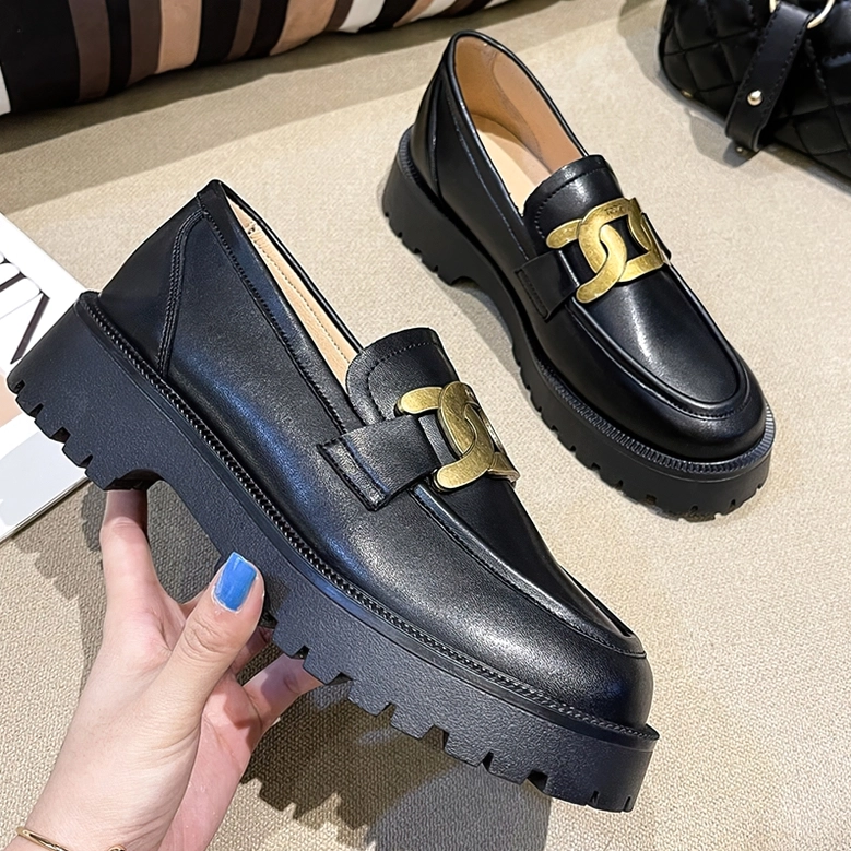 Black gothic platform loafers held by decorated hand in flat lay and three-quarter angle, showcasing smooth leather texture, metallic chain accent, and substantial outsole construction