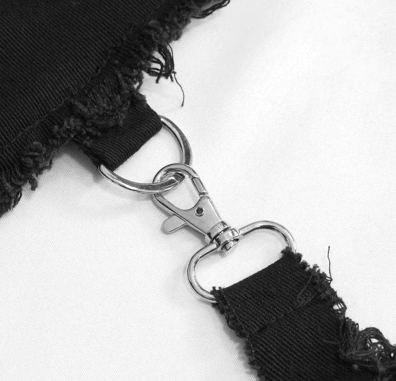 Metal chain and frayed black fabric detail on gothic asymmetrical pants, close-up shot showing hardware