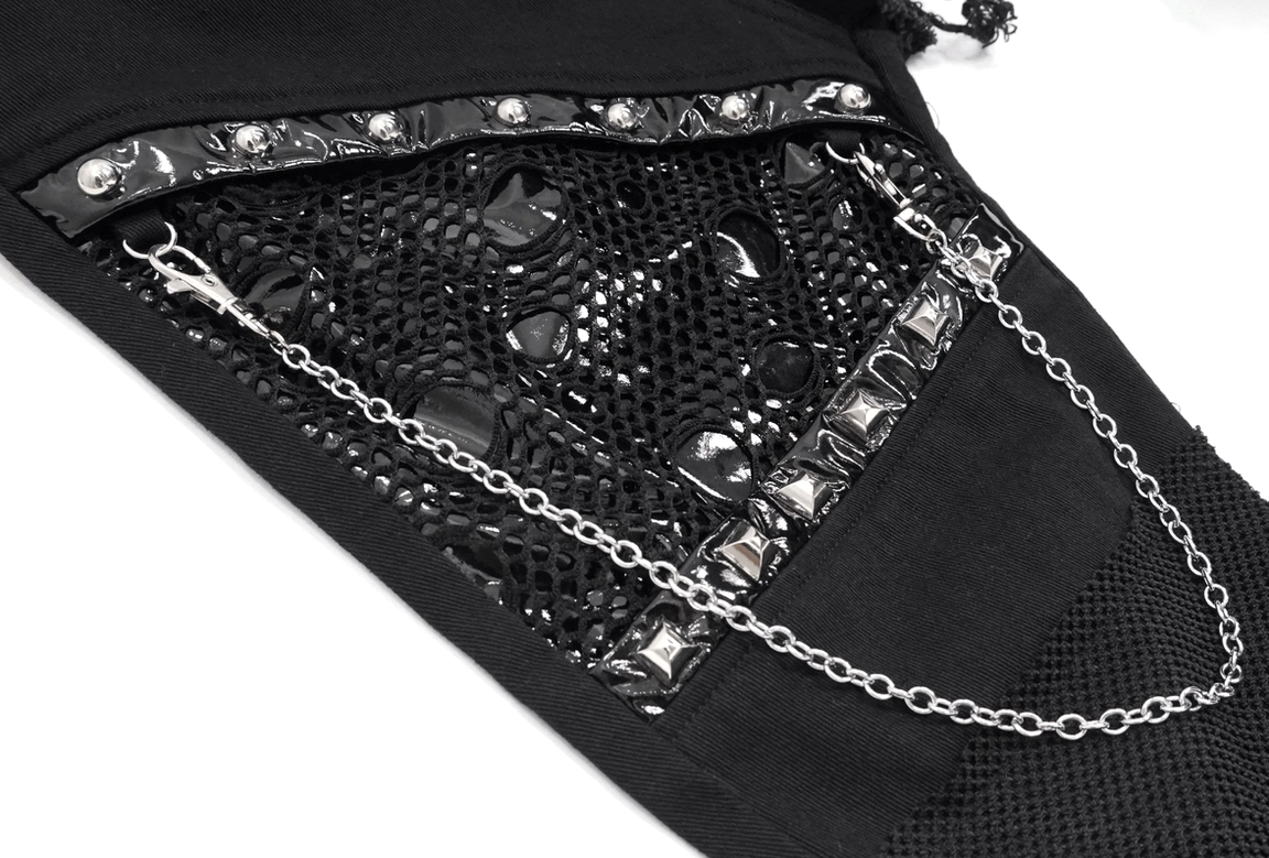 Studded mesh patch and silver chain detail on black gothic trousers, architectural design close-up