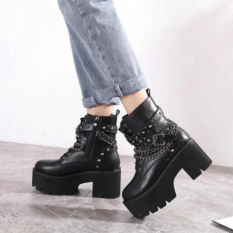 Low side profile of woman wearing black gothic platform ankle boots showing chunky platform sole and chain stud decoration in indoor setting