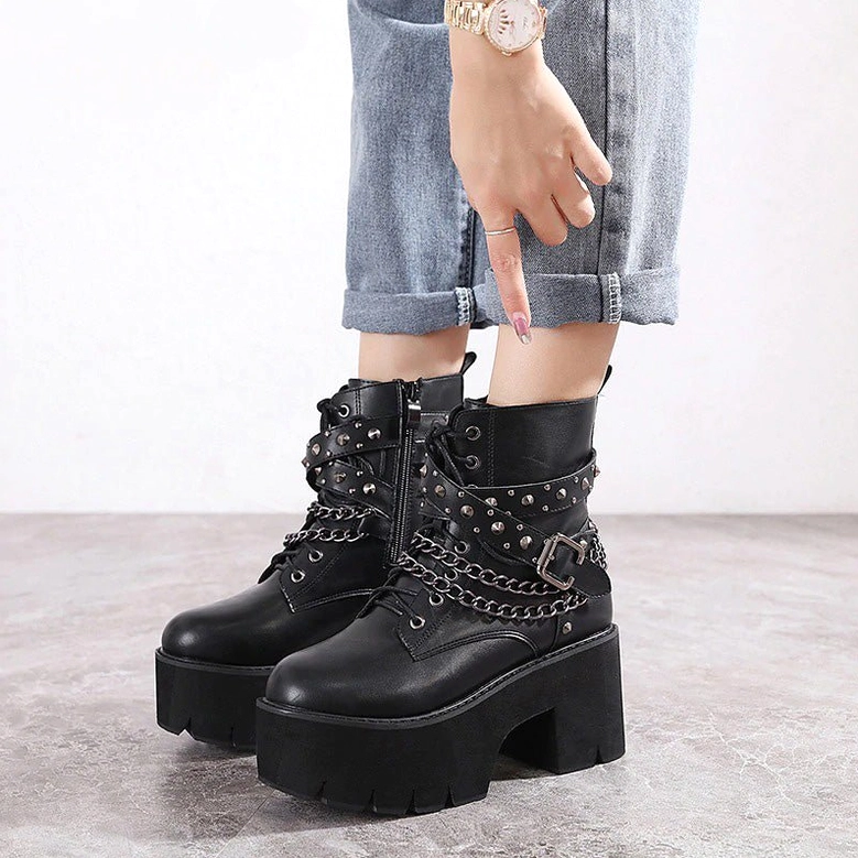 Woman wearing black gothic platform ankle boots with cropped jeans on marble floor, front side angle showing lace-up and chain details
