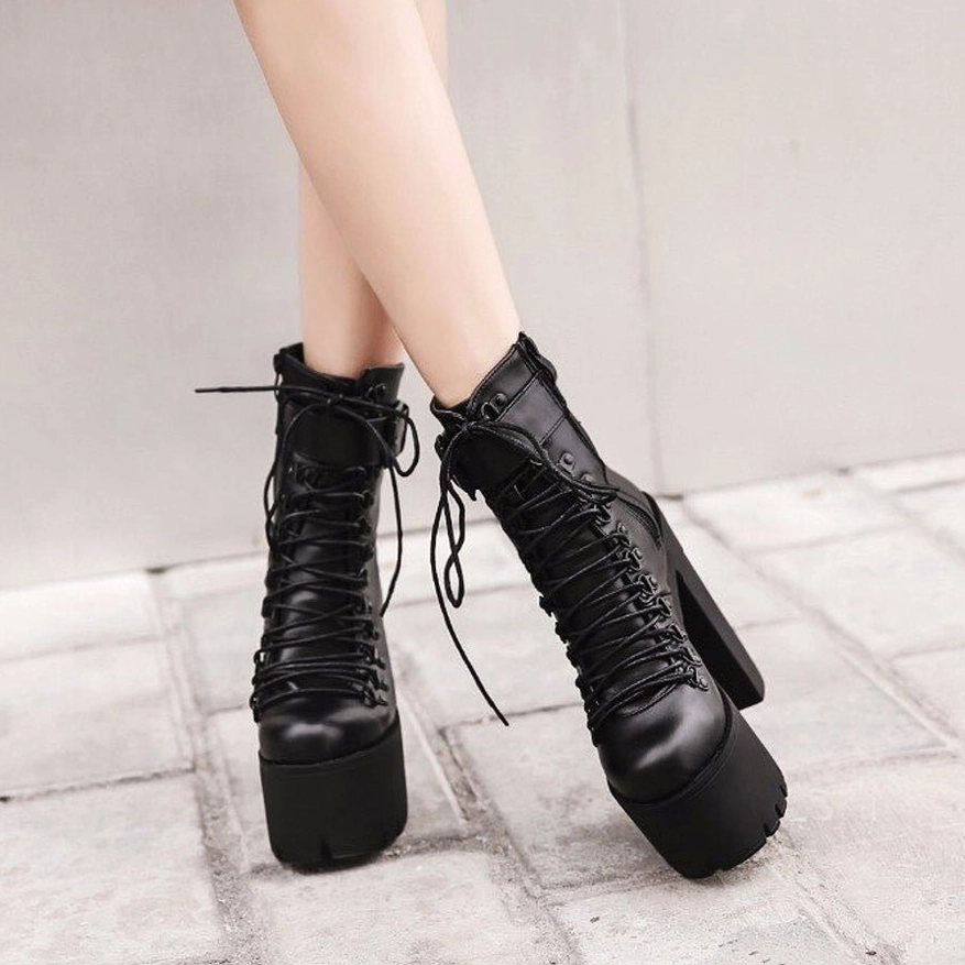 Black lace-up gothic platform boots worn on female feet outdoor tiled ground showing full silhouette