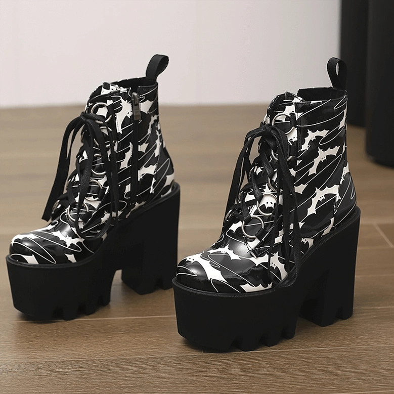 Pair of black bat print gothic platform ankle boots on wooden floor, front three-quarter view showcasing matching lace-up fastenings and chunky heels