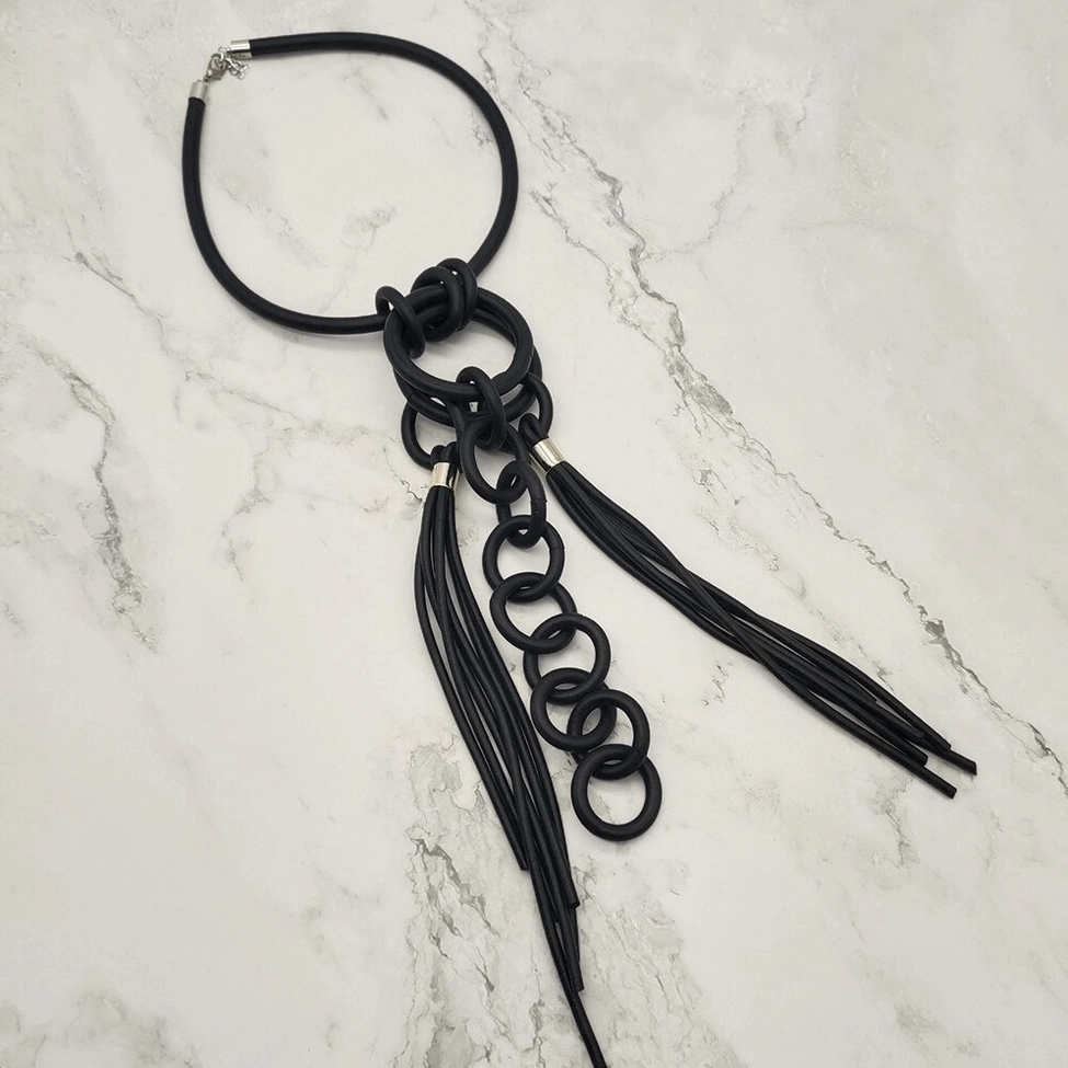 Long black rubber gothic necklace with linked rings and lobster claw clasp displayed on marble tabletop, alternative fashion jewelry