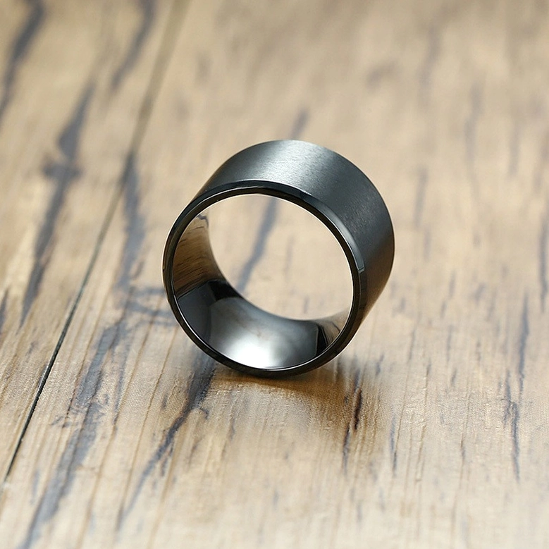Overhead oblique view of black gothic ring on wooden surface showing matte black finish and polished interior band