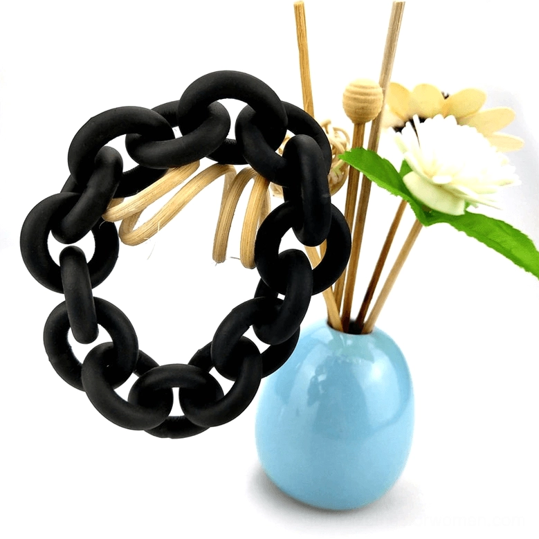 Black rubber geometric linked chain bangle on white background with floral reed diffuser, top-down flat lay product photography