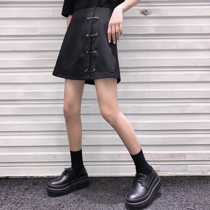 Black safety pin mini skirt styled with loafers and socks, full front model shot casual punk aesthetic