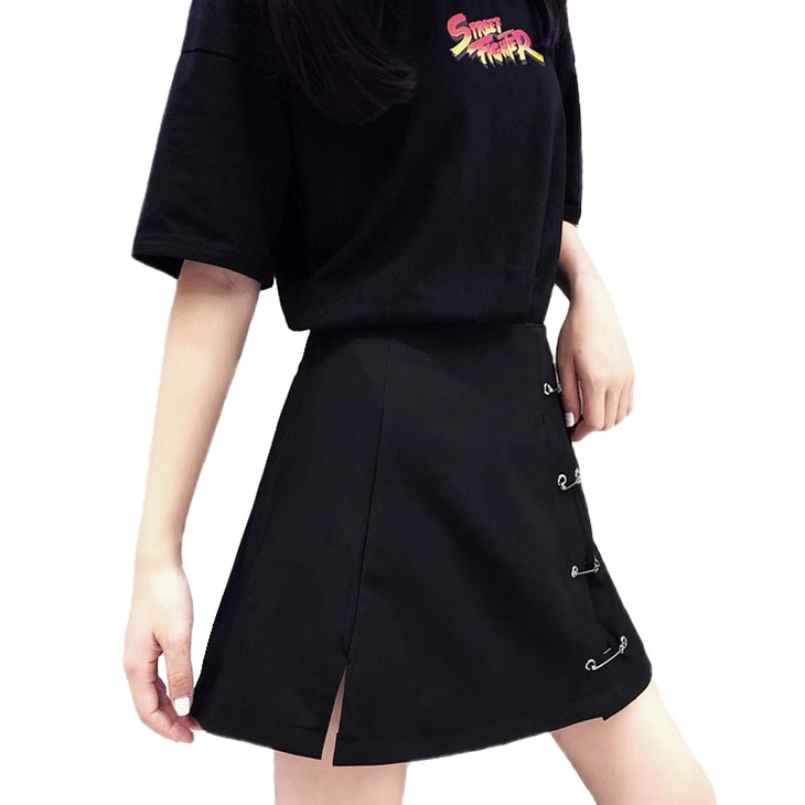 Black safety pin mini skirt styled with oversized black tee and side slit detail visible, casual indoor setting