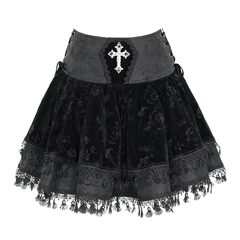 Flat lay front view of black velvet gothic mini skirt showing embroidered cross decor, side lace-up waist design, rose-patterned velvet texture, and ruffled lace tassel trim