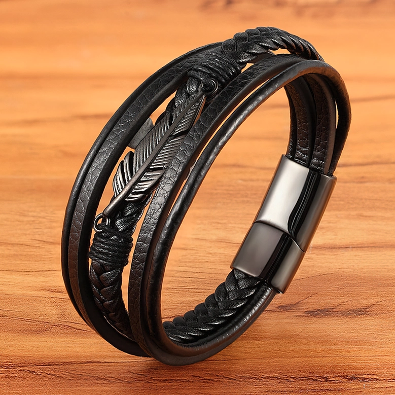 Black braided leather gothic bracelet with black feather charm, side oblique view on wooden surface