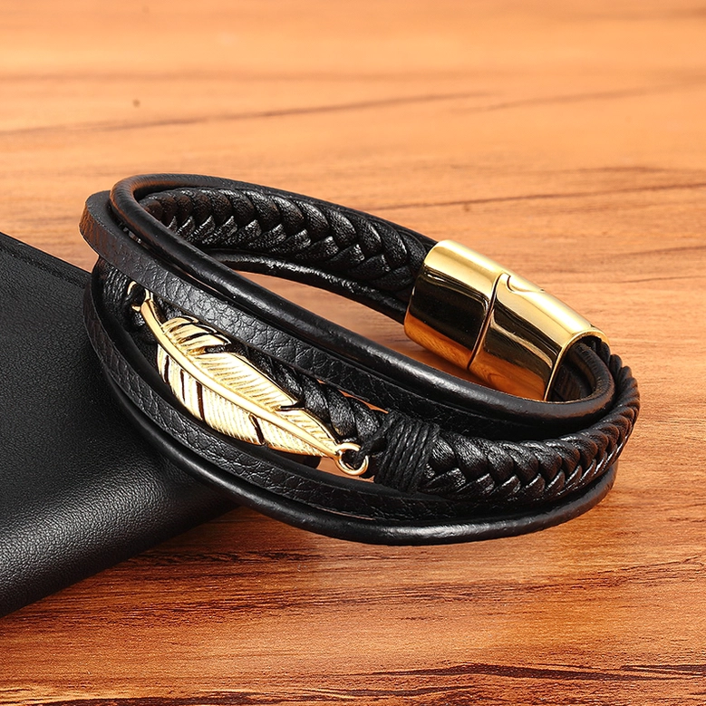 Gold feather black leather gothic bracelet detail shot, overhead view on wooden background with accessories