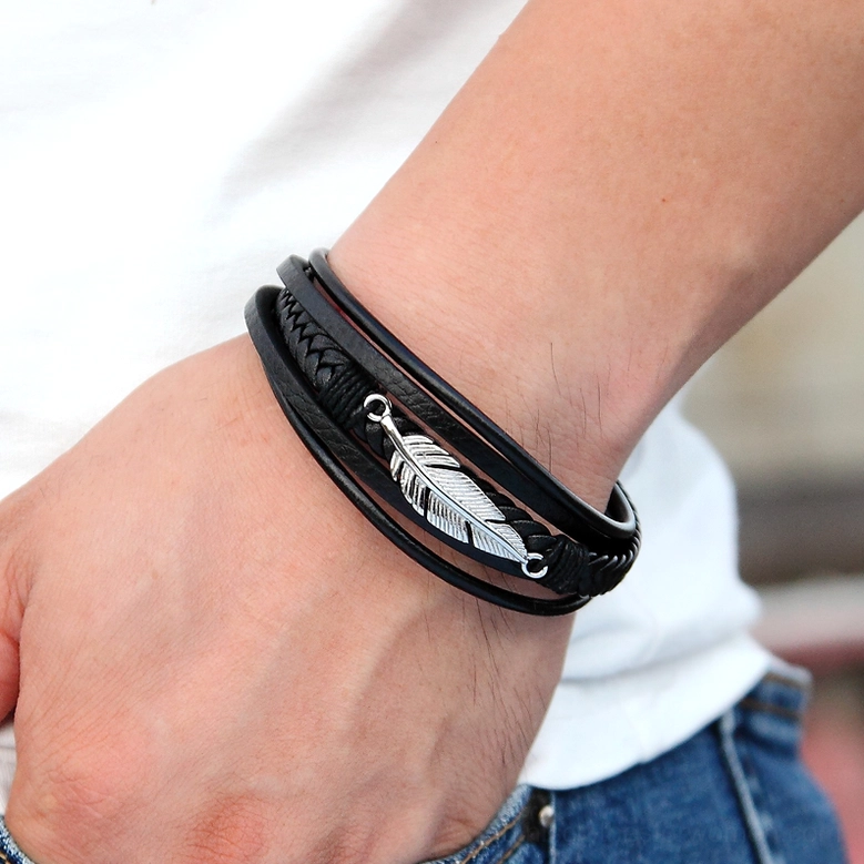 Silver feather black leather gothic bracelet worn on male wrist, close-up lifestyle photography showing fit