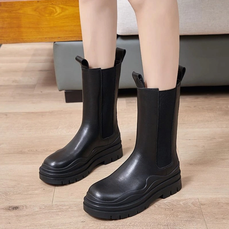 Woman in black leather platform boots with elastic side panels and pull tabs, front side view showing rounded toe design and top details