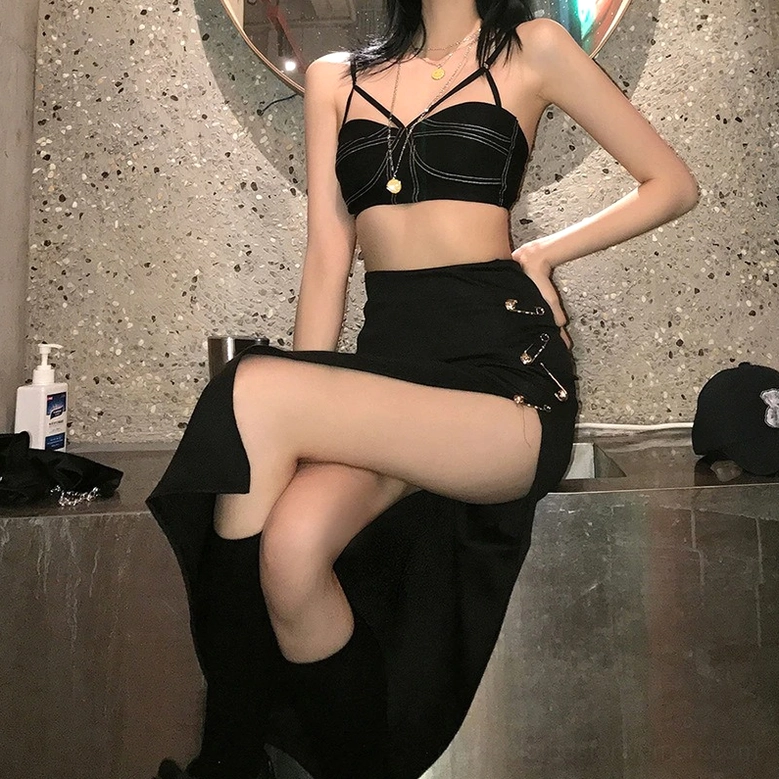 Black gothic midi skirt worn by model indoors showing dramatic side slit and safety pin decorations on cropped top styled look