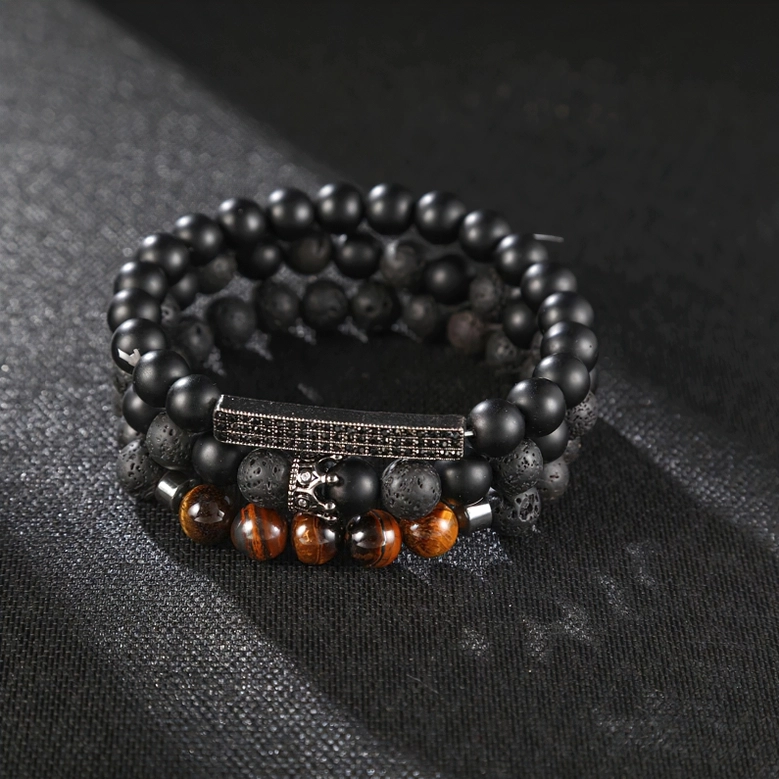 Flat lay top-down view of black onyx gothic bracelet with crown charm and tiger eye stone accents on dark fabric