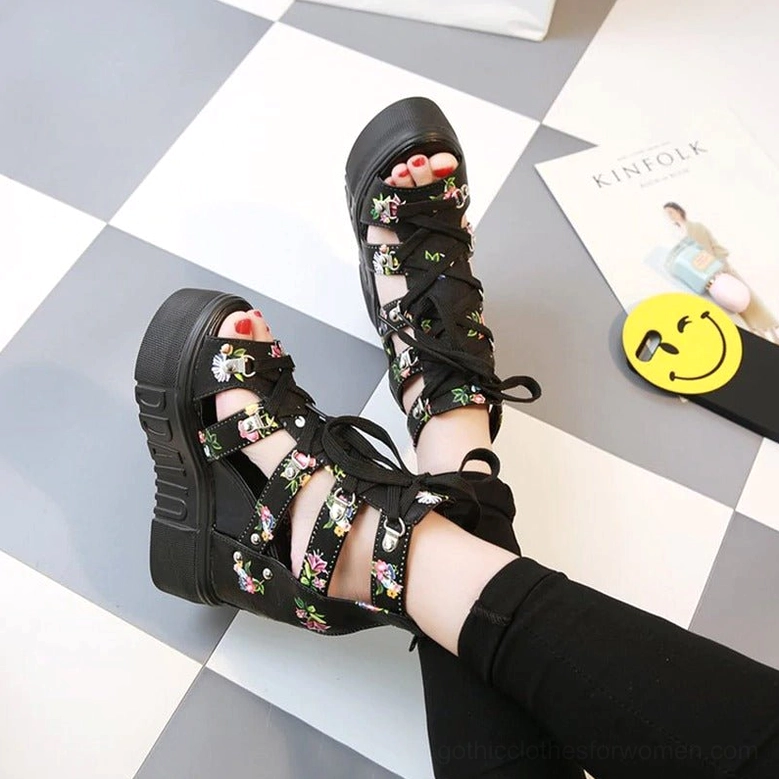 Black floral platform wedge sandals with open toe and lace-up details, top-down flat lay on checkered tile floor with decorative props